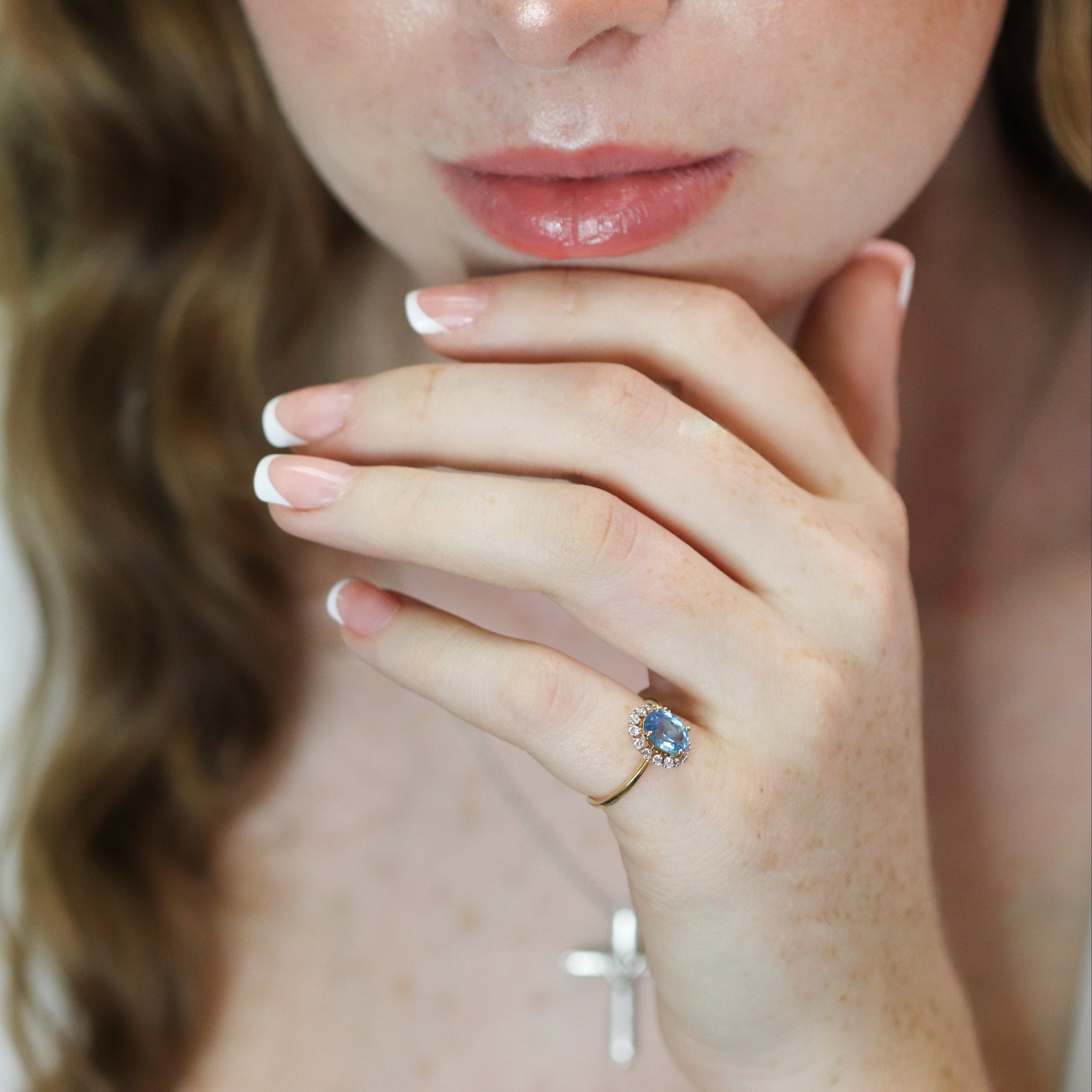 Close-up of a woman's hand wearing a ring with a diamond and blue topaz, against a blurred background.