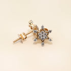 Gold star-shaped earrings with diamond-like stones on a beige background
