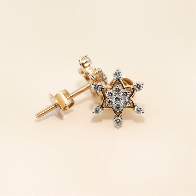 Gold star-shaped earrings with diamond-like stones on a beige background