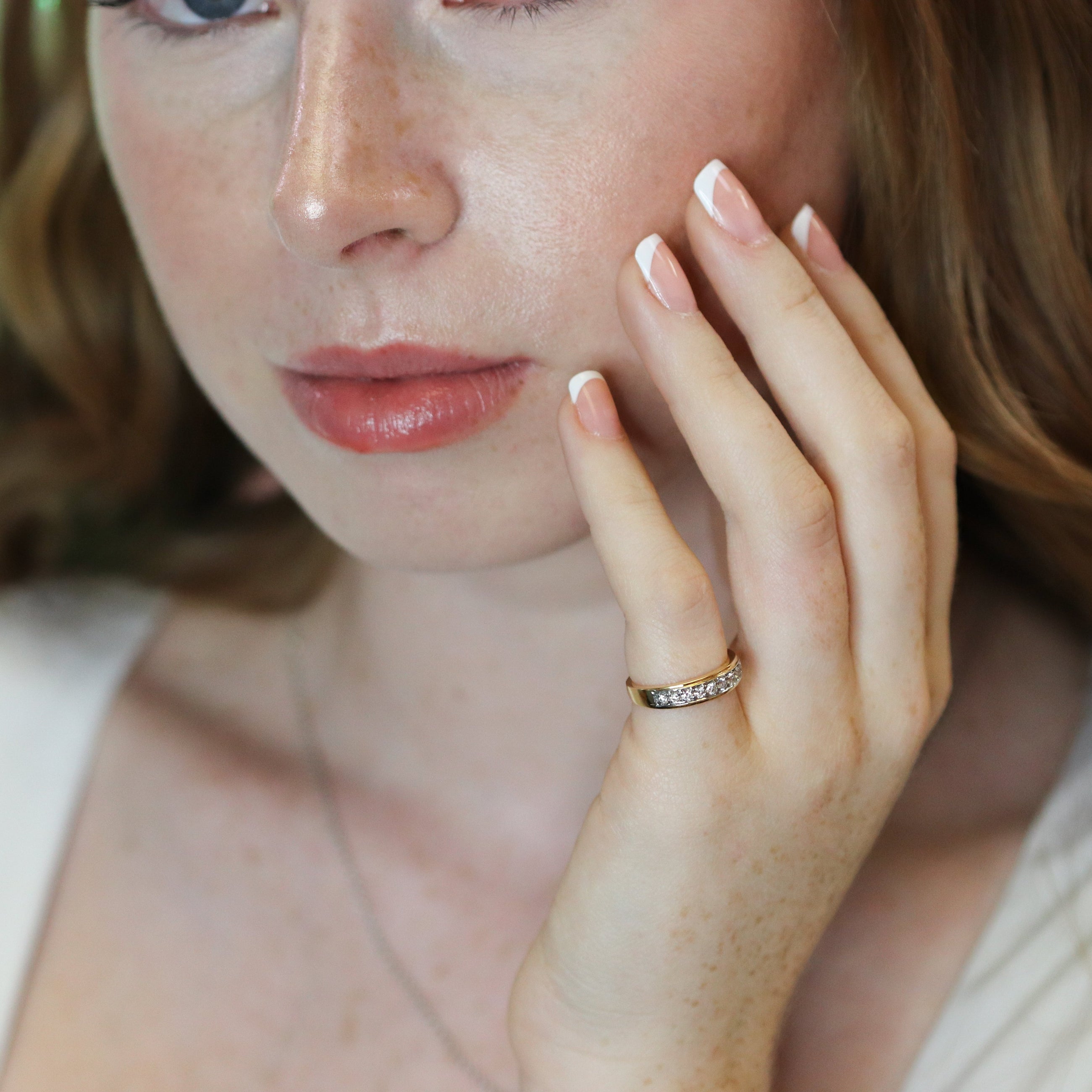 Woman with a ring on her finger touching her face against a pink background