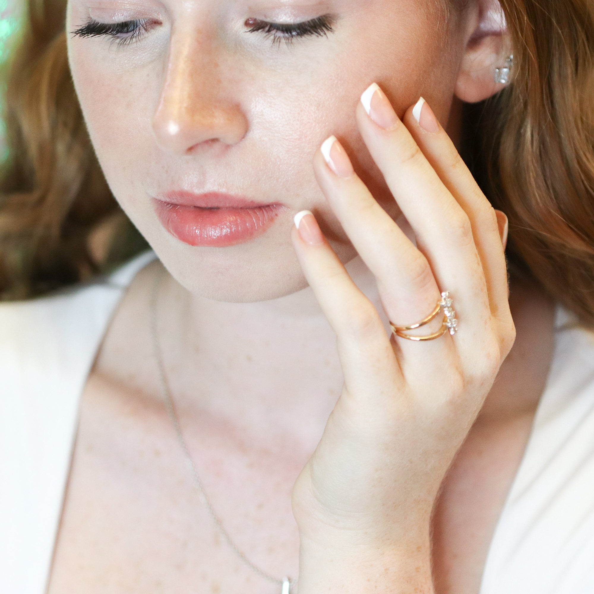 Woman with a diamond ring on her finger wearing a white top.