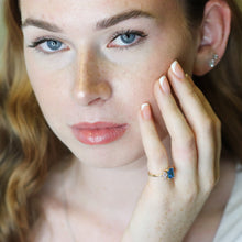 Woman wearing a ring with a blue gemstone, close-up of face and hand.